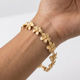 11mm 14k Plumeria Bracelet with 13 diamonds and 13 flowers — studio macro closeup on model (brunette)